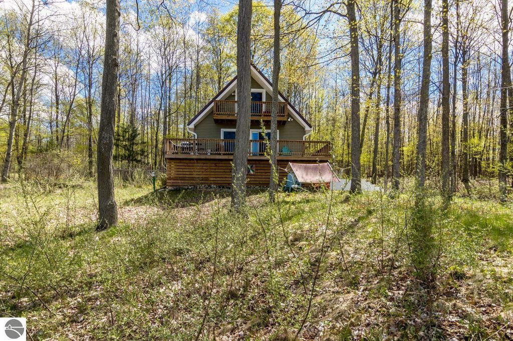 Chalet style home surrounded by trees on 5 acres, featuring a deck and peaceful natural setting near Torch Lake in Alden, MI.