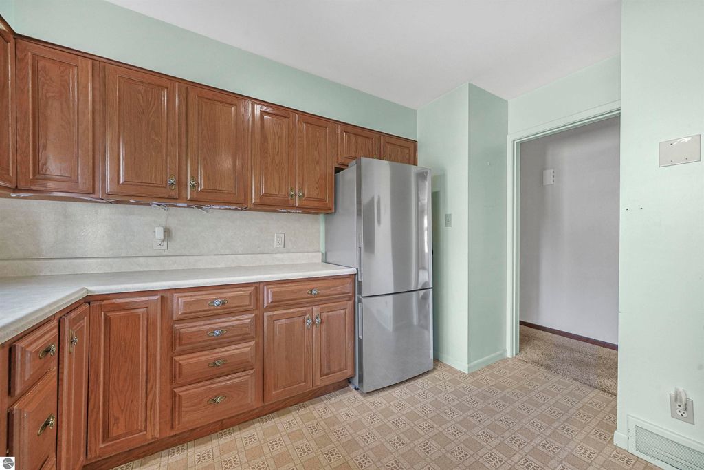 Kitchen interior featuring wooden cabinetry, stainless steel refrigerator, and light green walls in a ranch-style home at 315 N Simons Street, Cadillac, MI.