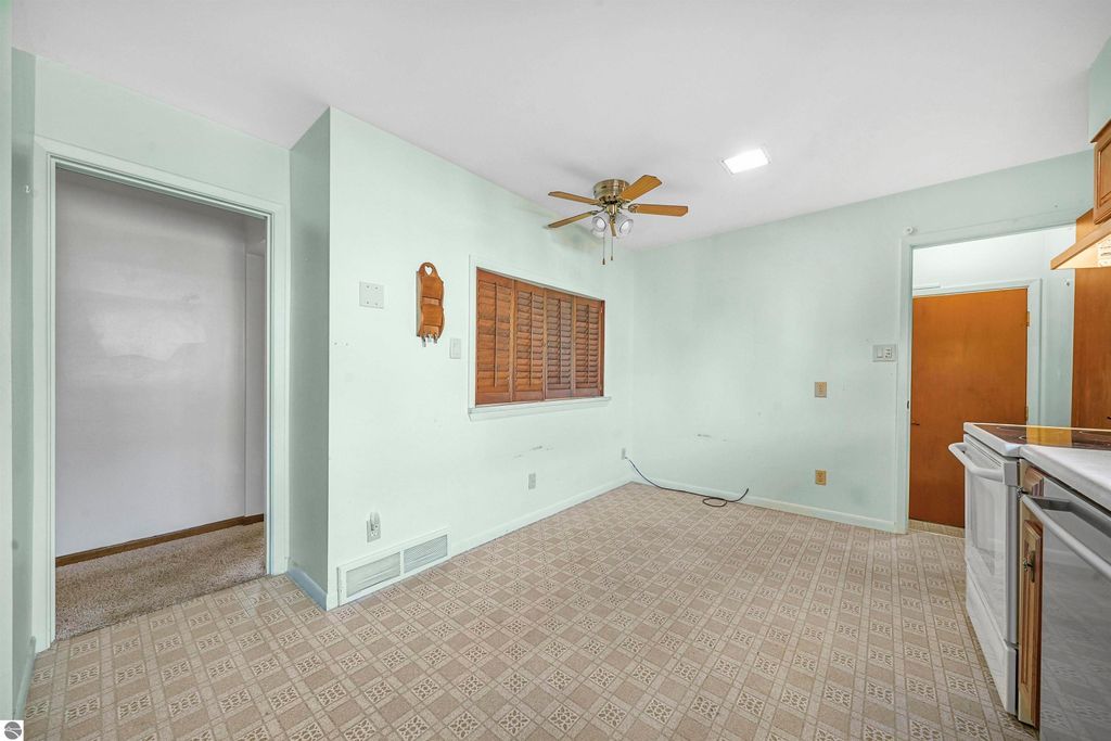 Interior view of a cozy kitchen area in a 3-bedroom ranch home for sale in Cadillac, MI, featuring light green walls, a ceiling fan, and a window with wooden shutters, showcasing the property's potential for comfortable living.