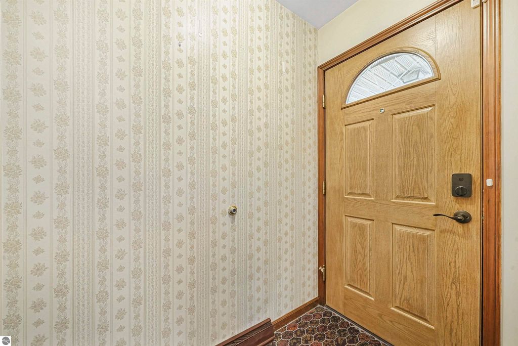 Entryway of a ranch-style home at 315 N Simons Street, Cadillac, MI, featuring a wooden front door, floral patterned wallpaper, and textured flooring.