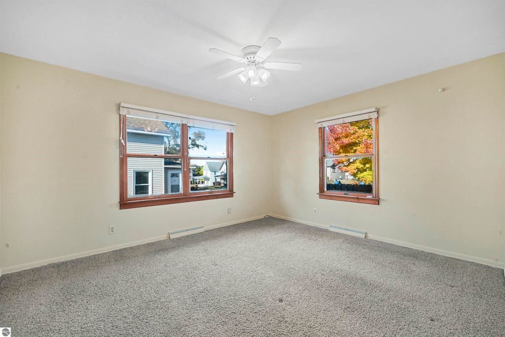 Spacious living room with large windows, ceiling fan, and neutral carpet, showcasing natural light and views of the surrounding neighborhood, ideal for the 3-bedroom, 2-bath ranch at 315 N Simons Street, Cadillac, MI.
