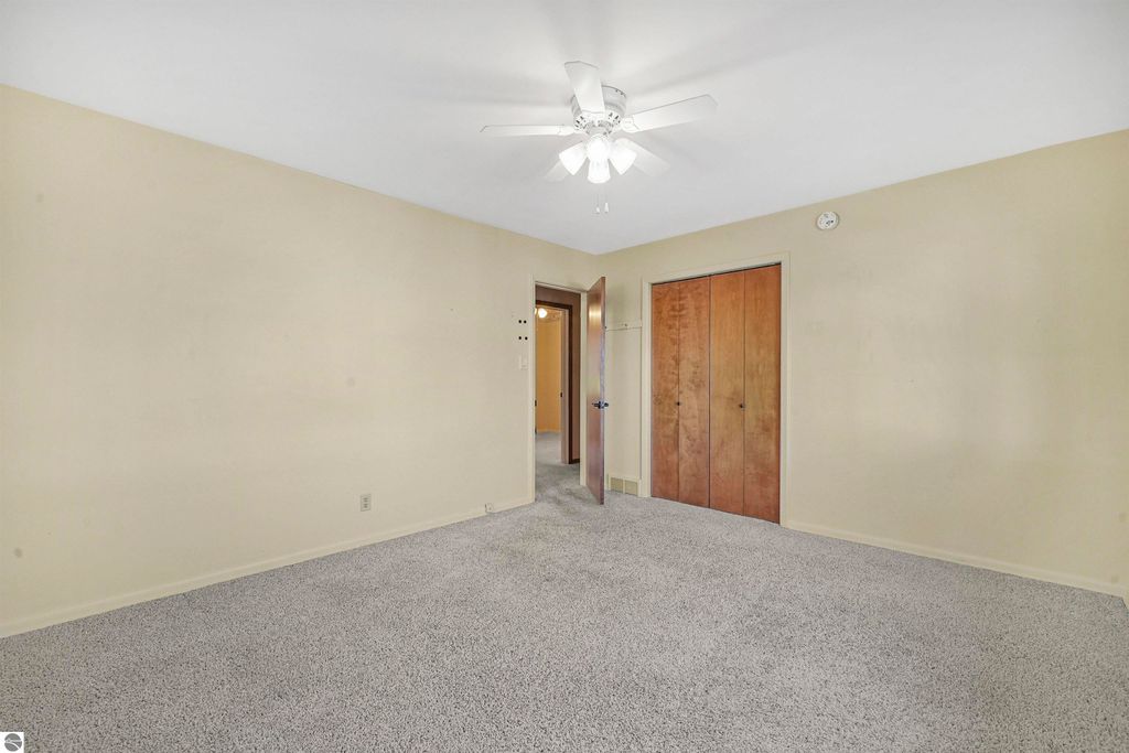 Spacious interior of a 3-bedroom ranch home in Cadillac, featuring beige walls, carpeted flooring, ceiling fan, and double closet doors, highlighting the cozy living space.