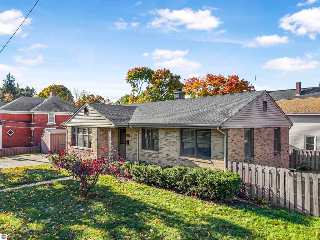 Charming ranch-style home at 315 N Simons Street, Cadillac, MI, featuring a brick exterior, landscaped yard, and fenced backyard, surrounded by autumn foliage.