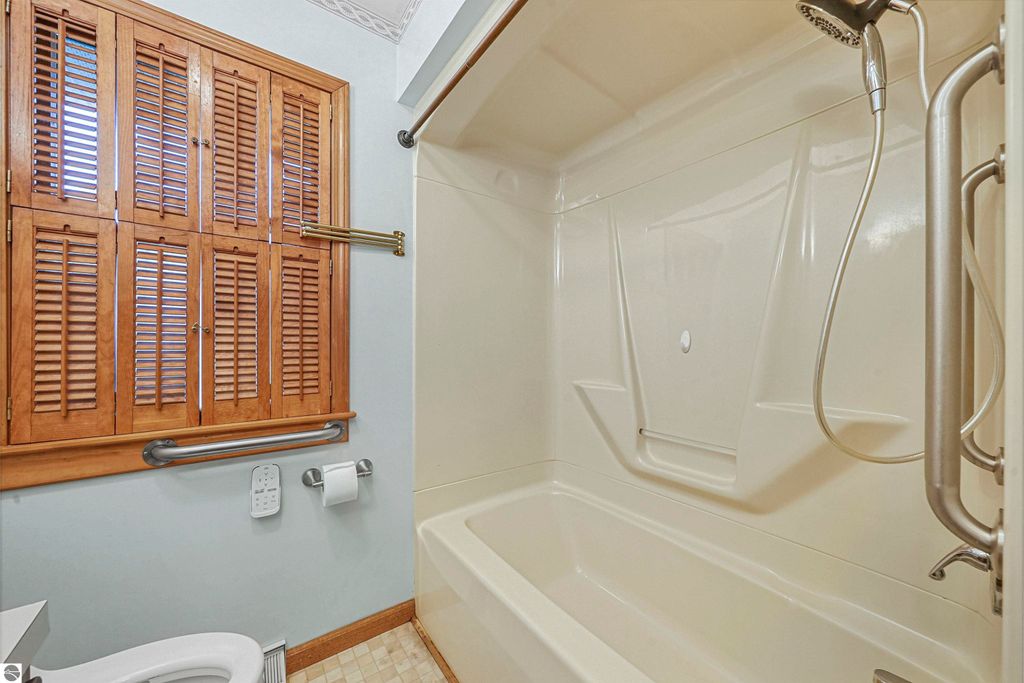 Bathroom featuring a shower-tub combination, wooden shutters, grab bars, and a clean, well-maintained appearance, highlighting the property's charm at 315 N Simons Street, Cadillac, MI.