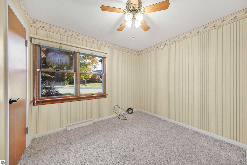 Cozy interior of a 3-bedroom ranch home in Cadillac, featuring a carpeted room with a ceiling fan, large windows, and decorative wallpaper.