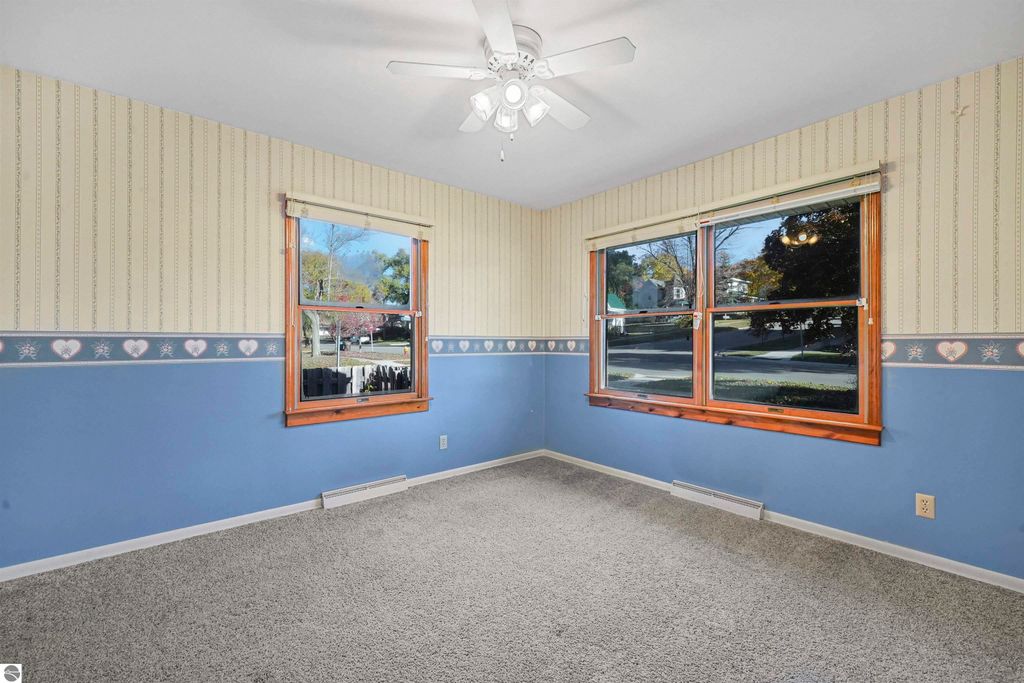 Cozy living room with blue and beige wallpaper, two large windows providing natural light, and a ceiling fan, showcasing the interior of the 3-bedroom, 2-bath home at 315 N Simons Street, Cadillac, MI.