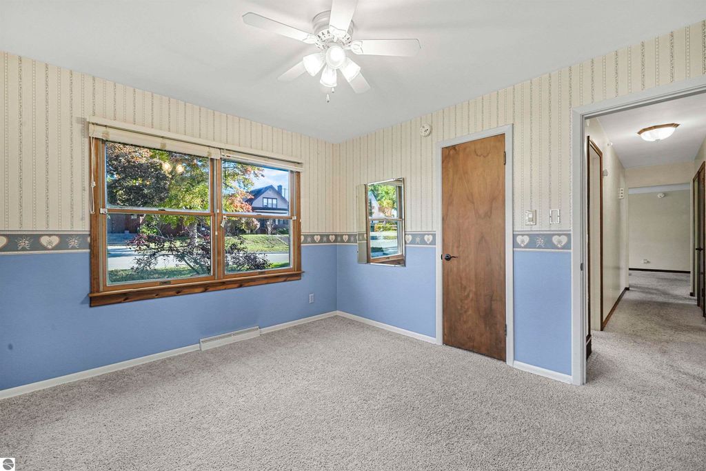 Cozy interior of a ranch-style home featuring blue and beige walls, large windows with natural light, and a door leading to a hallway, showcasing the living space at 315 N Simons Street, Cadillac, MI.