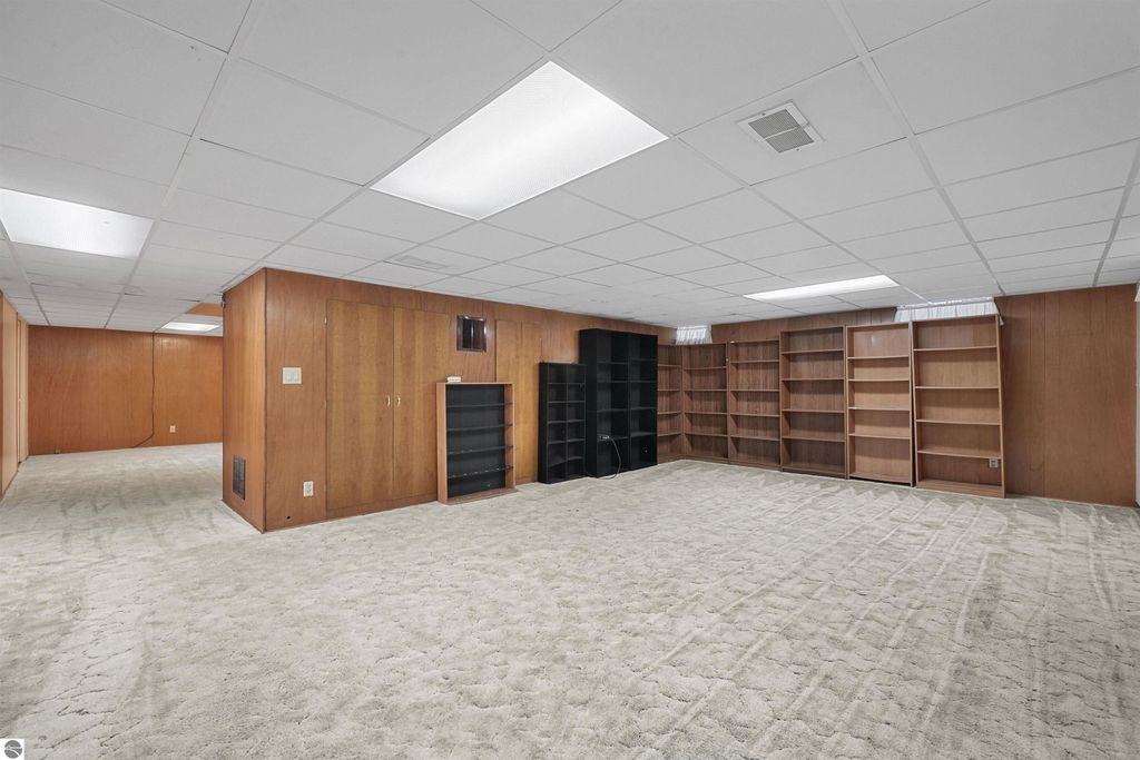Finished basement with carpeted flooring, wooden paneling, and built-in shelving units, showcasing additional living space for the property at 315 N Simons Street, Cadillac, MI.