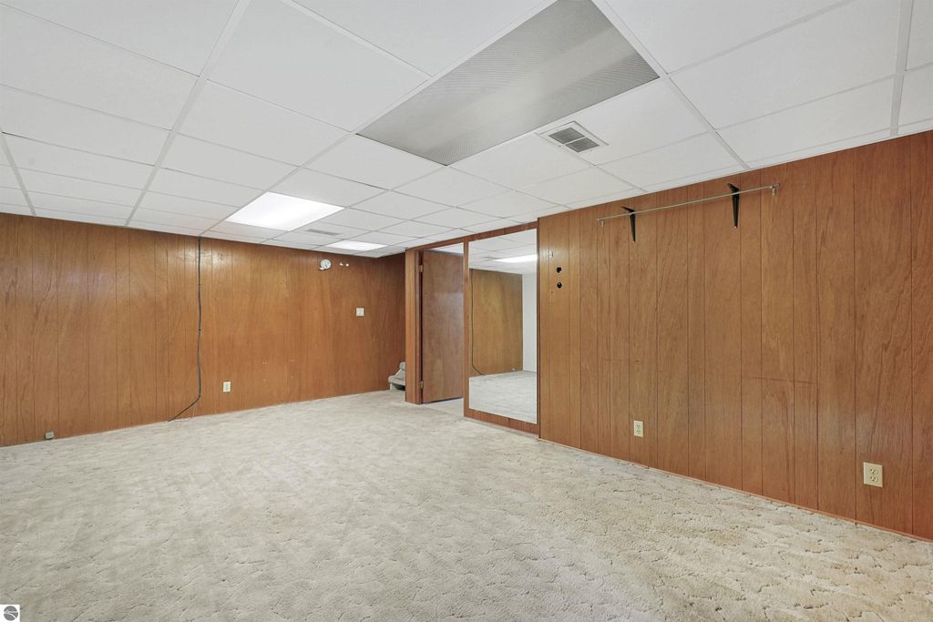 Finished basement space with beige carpet, wood-paneled walls, and a mirrored wall, showcasing additional living area in a Cadillac, MI home listing.