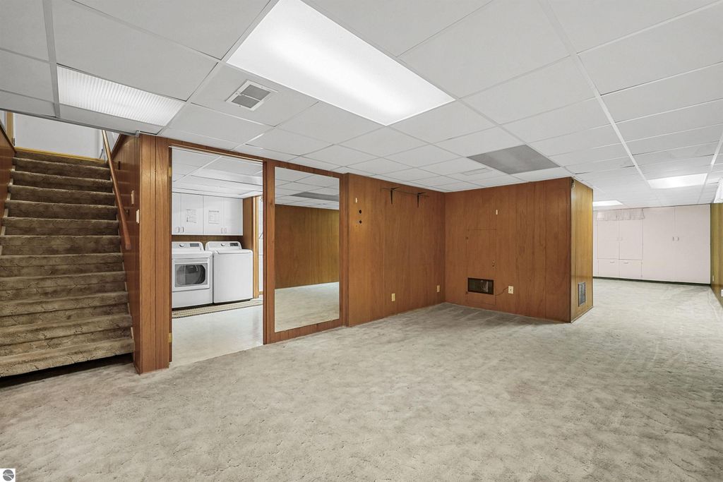 Finished basement with laundry area, carpeted floor, and wooden paneling, featuring staircase access and ample storage space in a Cadillac, MI home.