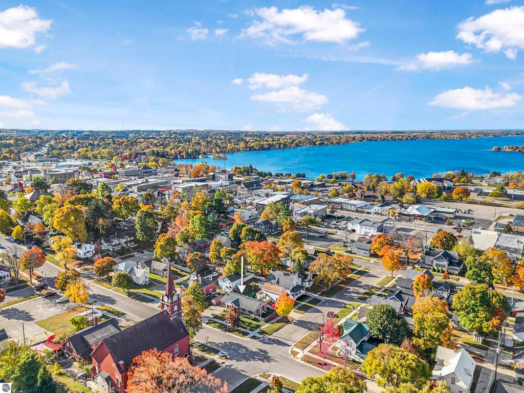 Aerial view of Cadillac, MI showcasing vibrant fall foliage, Lake Cadillac, and the surrounding residential and commercial areas, emphasizing the community's charm and proximity to nature.