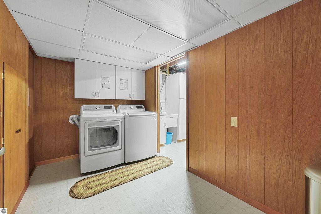 Laundry area in a finished basement featuring white washer and dryer, wooden paneling, storage cabinets, and a cozy rug, highlighting additional living space in the 3-bedroom ranch home at 315 N Simons Street, Cadillac, MI.