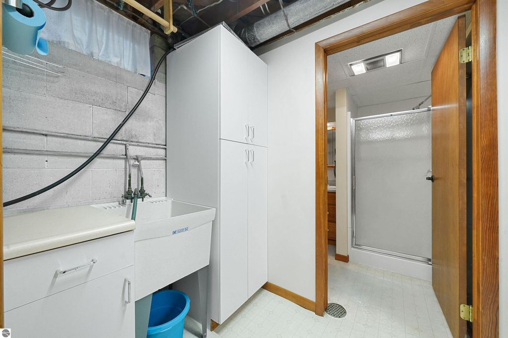 Basement laundry area featuring a utility sink, storage cabinets, and a shower stall, highlighting the functional space in the home at 315 N Simons Street, Cadillac, MI.