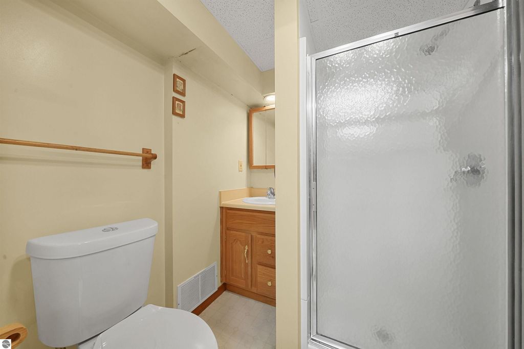 Bathroom interior featuring a toilet, vanity with sink, and a glass shower stall in a well-maintained ranch home for sale in Cadillac, MI.