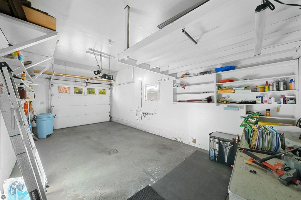 Spacious garage interior with storage shelves, organized tools, and a blue trash bin, showcasing the property at 315 N Simons Street, Cadillac, MI.