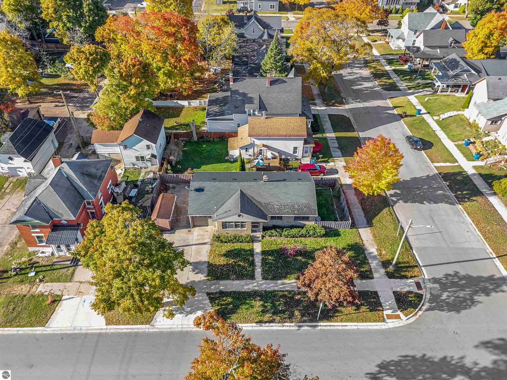 Aerial view of a charming ranch-style home at 315 N Simons Street, Cadillac, MI, featuring a fenced backyard, nearby trees with autumn foliage, and surrounding residential neighborhood.