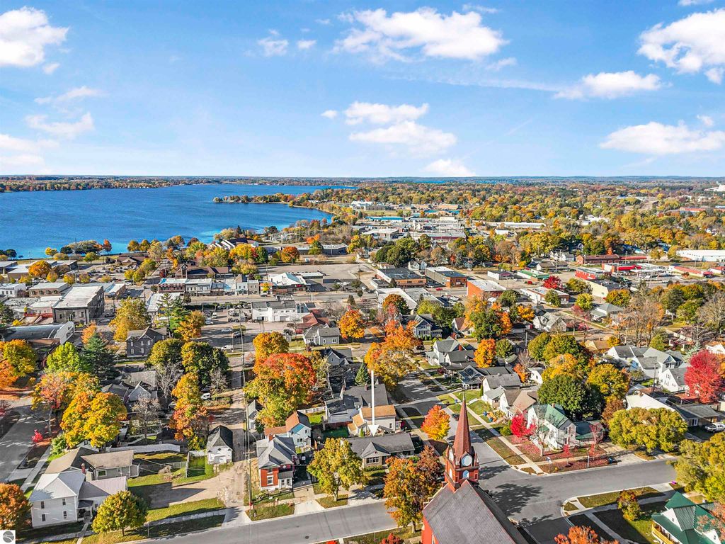 Aerial view of Cadillac, MI showcasing colorful autumn foliage, Lake Cadillac, and the downtown area with residential homes and commercial buildings.