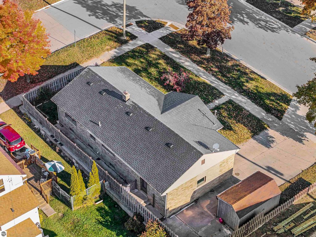 Aerial view of a charming ranch-style home at 315 N Simons Street, Cadillac, MI, showcasing a fenced backyard, attached garage, and nearby colorful autumn trees.