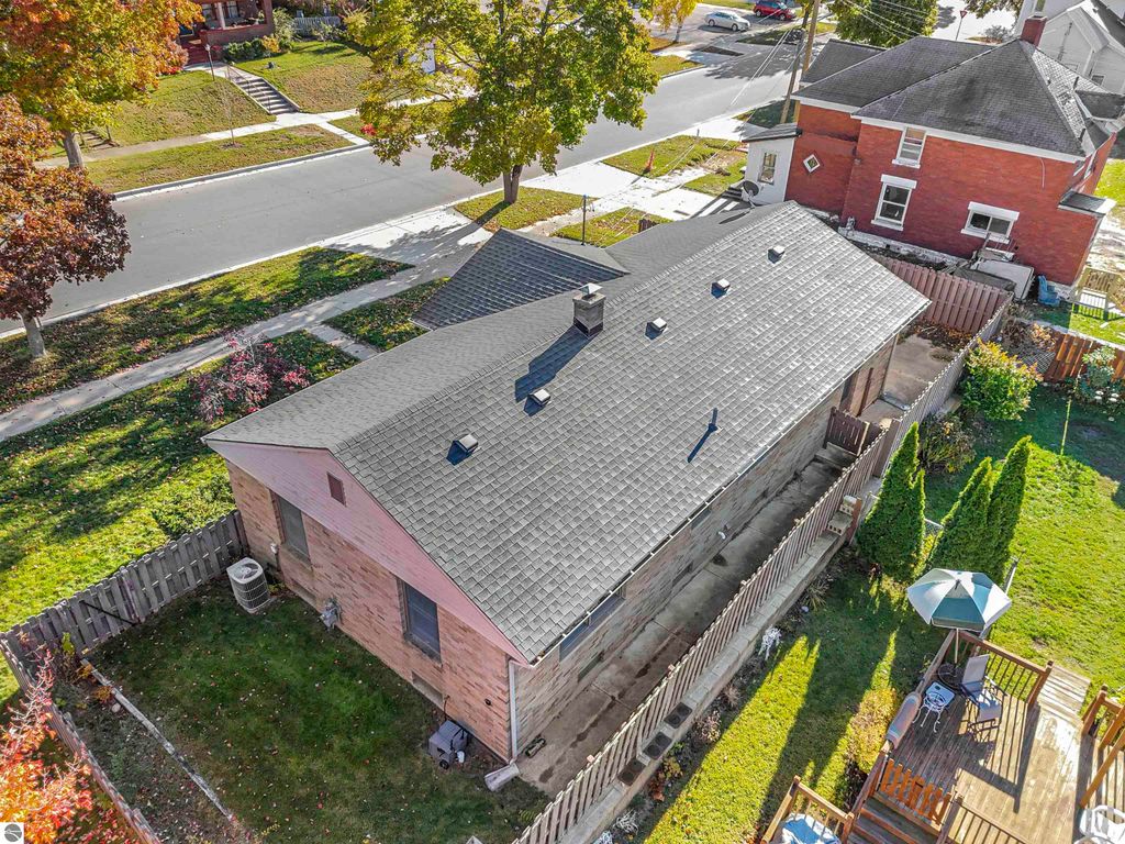 Aerial view of a charming ranch-style home with a new roof, surrounded by a fenced backyard and nearby landscaping, located at 315 N Simons Street, Cadillac, MI.