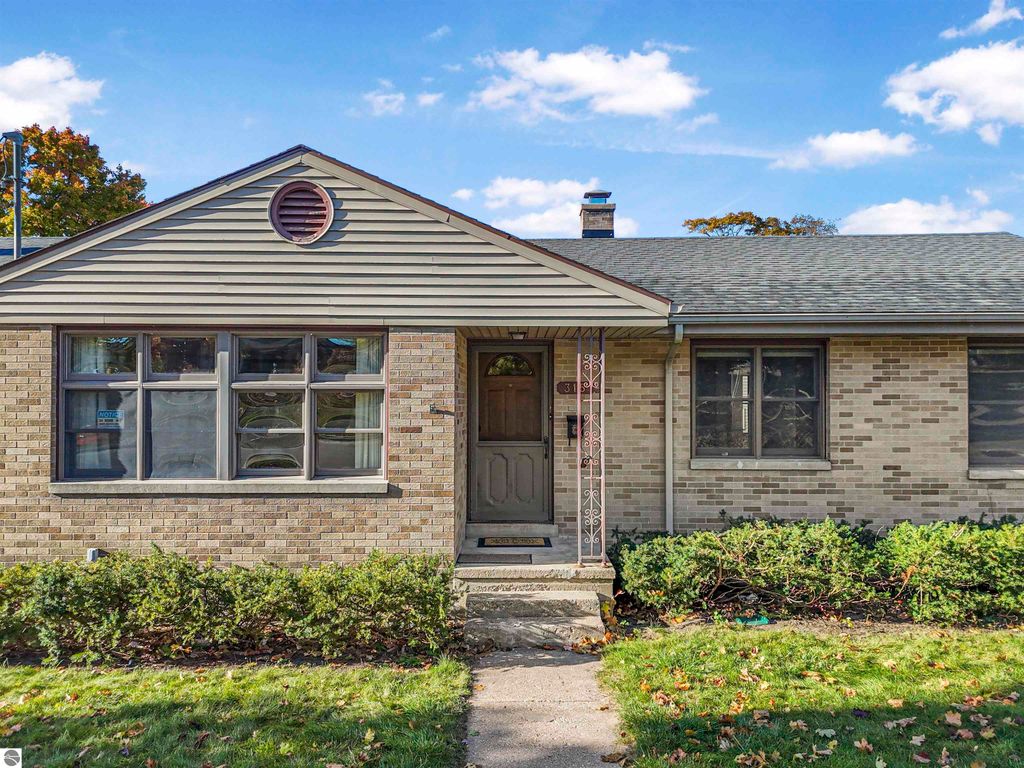 Charming ranch-style home at 315 N Simons Street, Cadillac, MI, featuring a brick exterior, large front windows, and a welcoming entryway, surrounded by landscaped greenery.