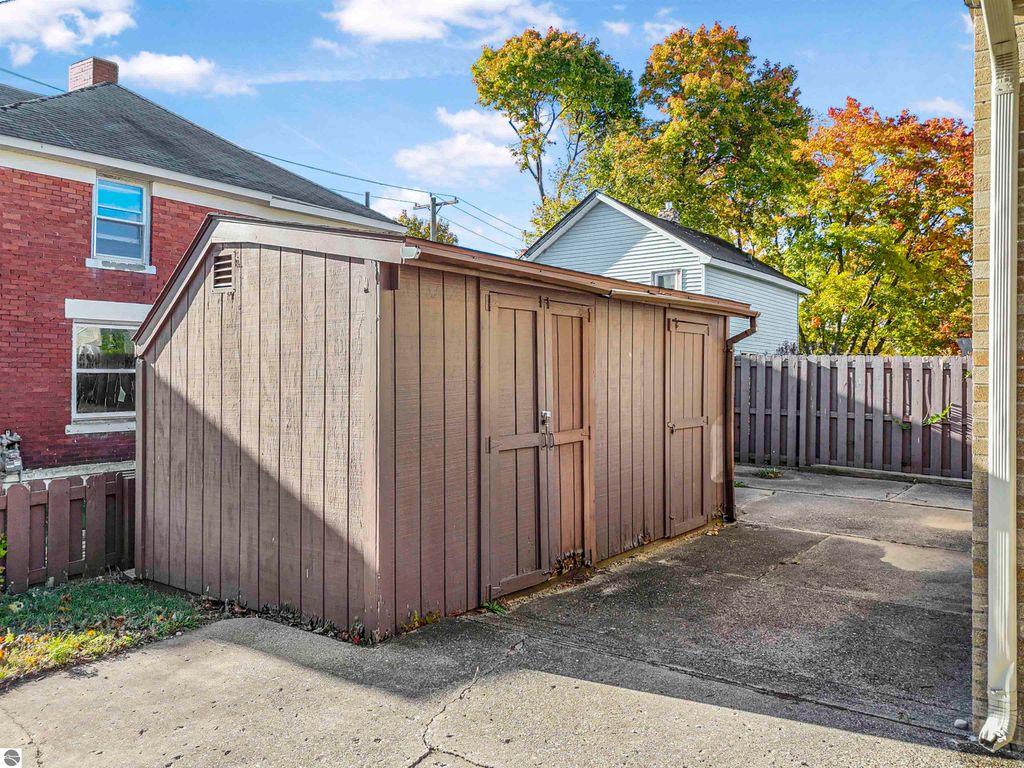Storage shed in fenced backyard of 315 N Simons Street, Cadillac, MI, showcasing nearby residential homes and autumn foliage.