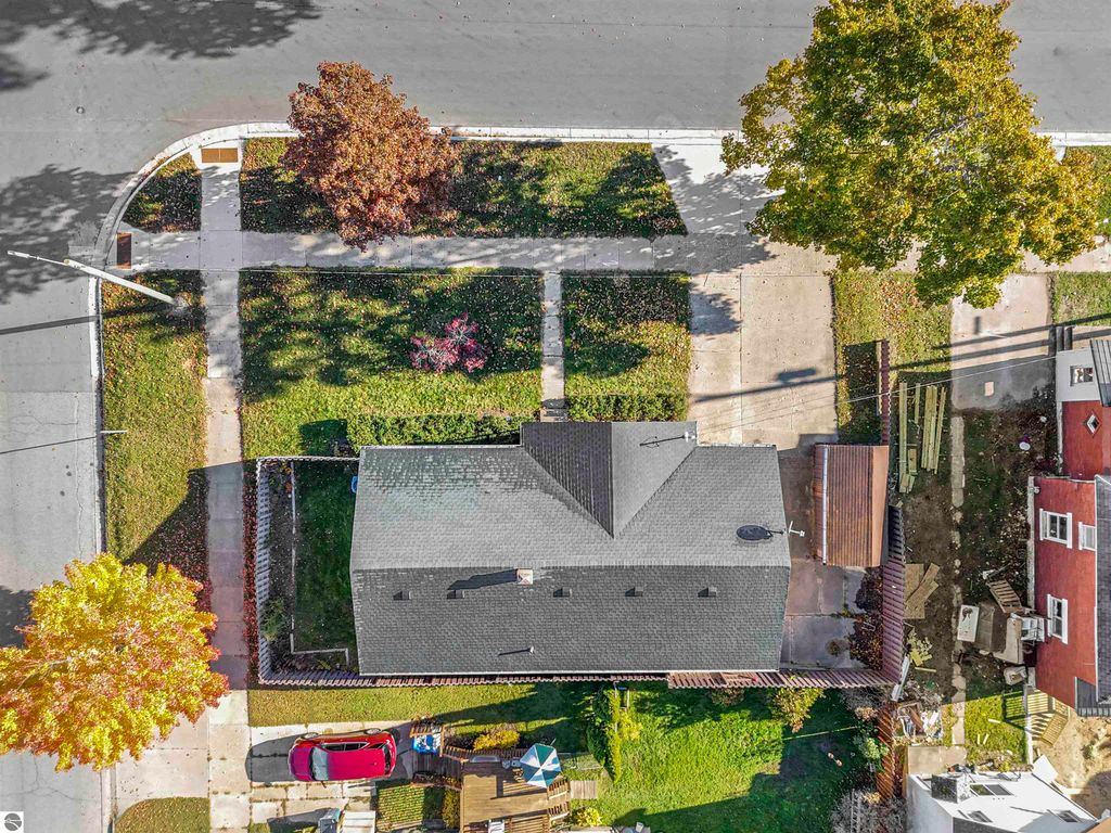 Aerial view of 315 N Simons Street, Cadillac, MI, showcasing the charming ranch-style home, fenced backyard, and surrounding neighborhood with trees and sidewalks.
