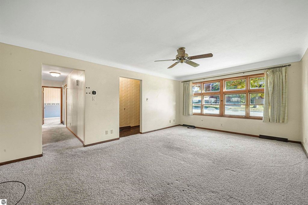 Cozy living room in a 3-bedroom ranch home at 315 N Simons Street, featuring large windows, ceiling fan, and neutral carpet, showcasing the inviting interior space.