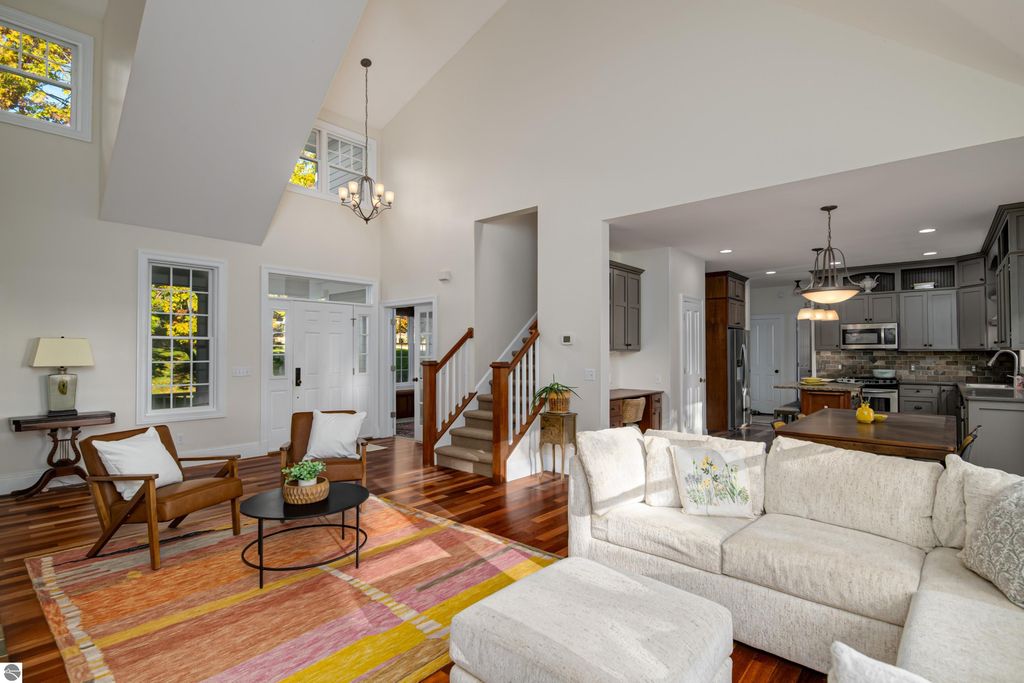 Bright, spacious interior of a modern home at 6436 Peregrin Court, featuring hardwood floors, a cozy living area with a white sectional sofa, stylish armchairs, and an open kitchen layout, highlighting natural light and elegant design elements.