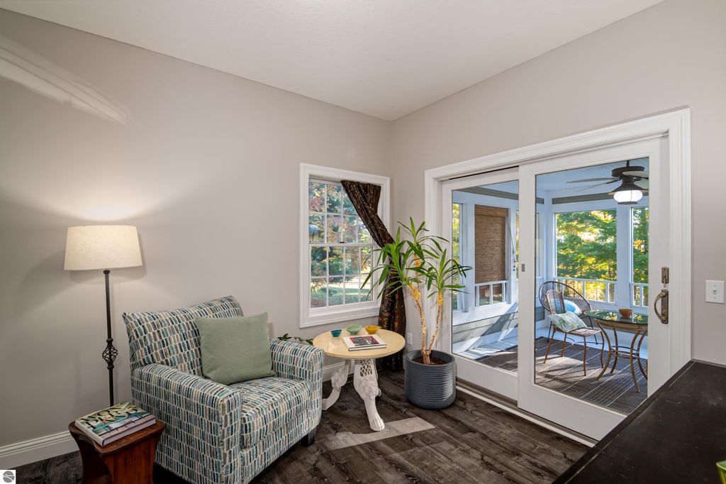 Cozy sunroom with seating area, decorative plant, and views of landscaped yard at 6436 Peregrin Court, Traverse City, MI.