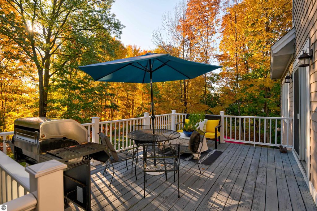 Deck with outdoor dining set, grill, and colorful umbrella, surrounded by vibrant autumn foliage, showcasing the scenic views near 6436 Peregrin Court, Traverse City, MI.