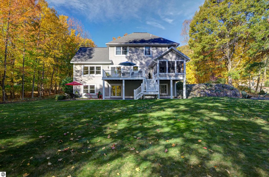 Custom-designed home at 6436 Peregrin Court, Traverse City, featuring a walkout lower level, expansive lawn, and surrounded by vibrant autumn foliage.