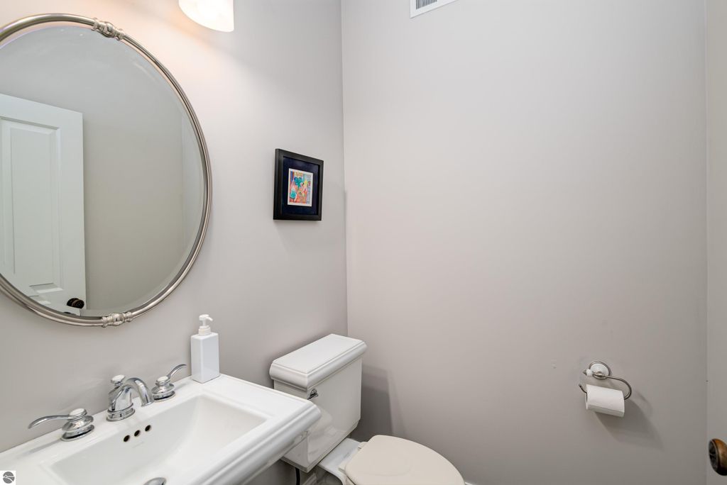 Bathroom with modern fixtures, circular mirror, and neutral wall color, featuring a white sink, toilet, and decorative artwork.