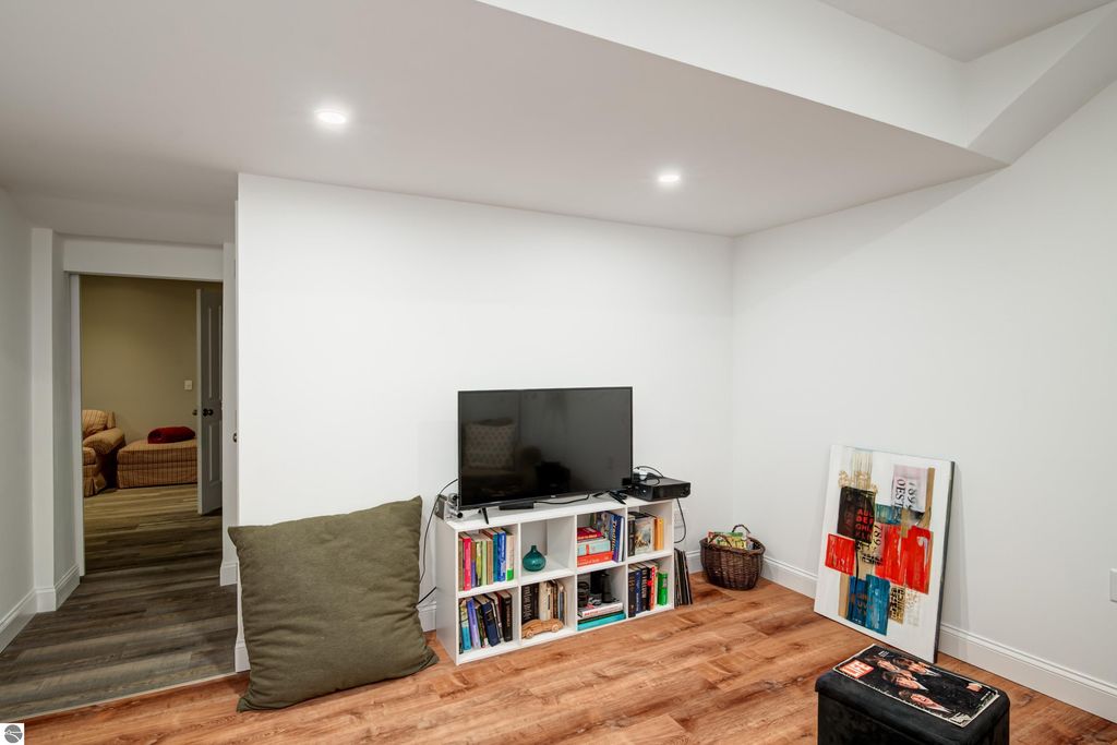 Cozy walkout lower level living space featuring a television, bookshelf, and decorative art, with a view into an adjacent room.
