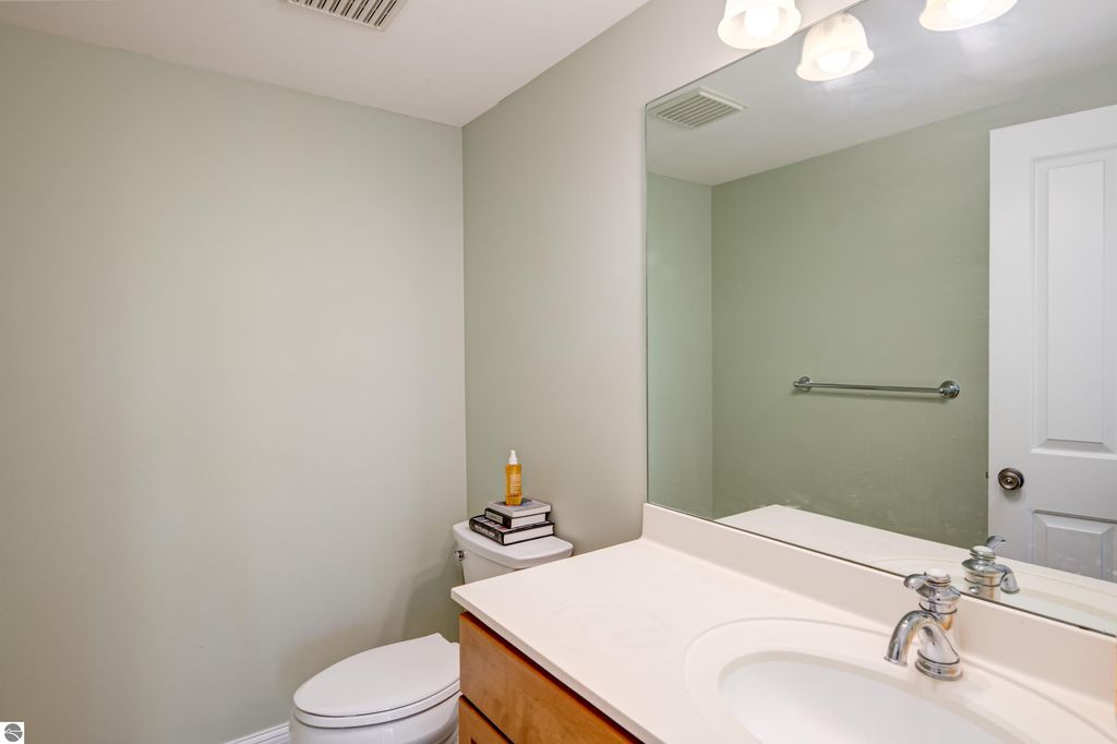 Modern bathroom interior with light green walls, white sink, and wooden cabinetry, featuring a mirror, towel bar, and toilet, showcasing a clean and inviting space.