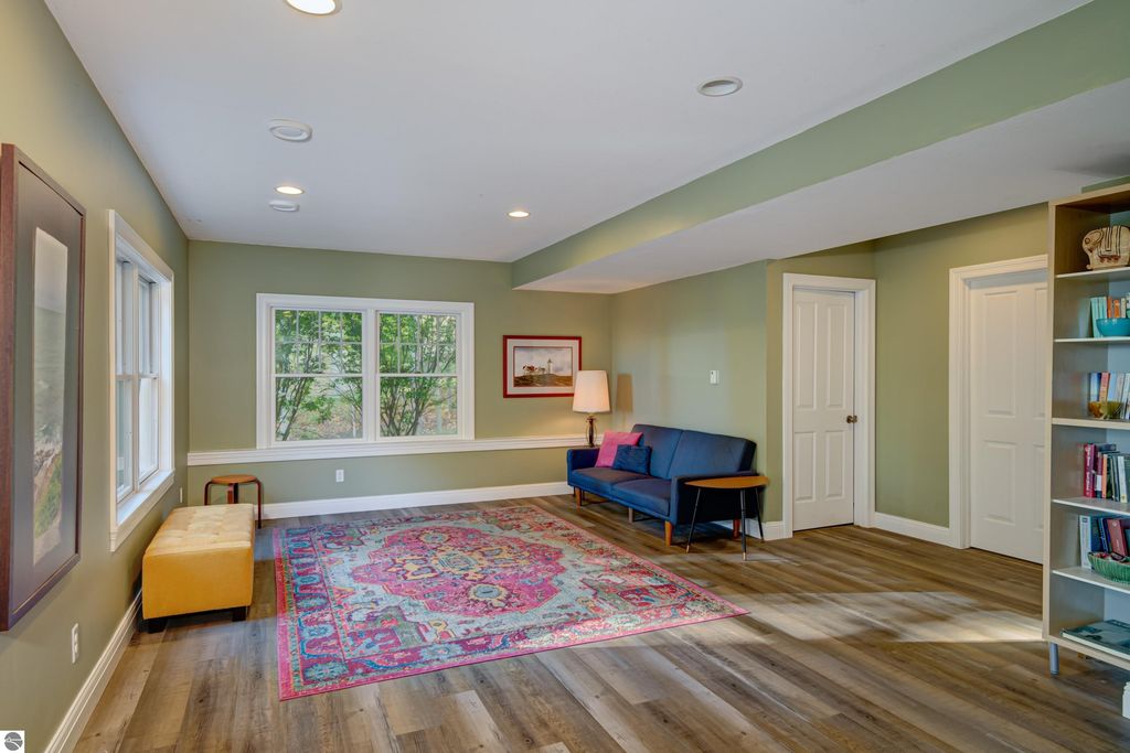 Cozy living space in Traverse City home featuring hardwood floors, large windows, and colorful area rug, ideal for relaxation and entertaining.