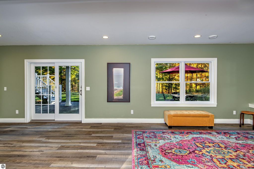 Interior view of a spacious living area at 6436 Peregrin Court, featuring large glass doors leading to a landscaped yard, a colorful area rug, and a cozy orange ottoman, capturing the blend of modern comfort and timeless architecture.