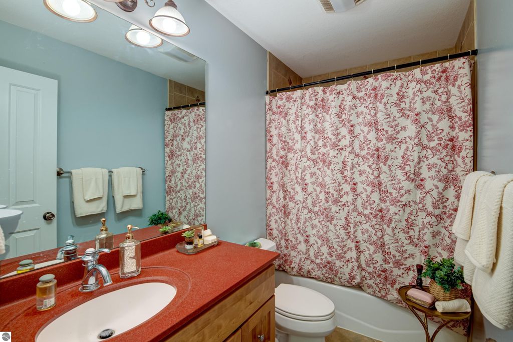 Bathroom interior featuring a red countertop sink, floral shower curtain, and modern fixtures, showcasing a blend of comfort and style in the Traverse City home at 6436 Peregrin Court.