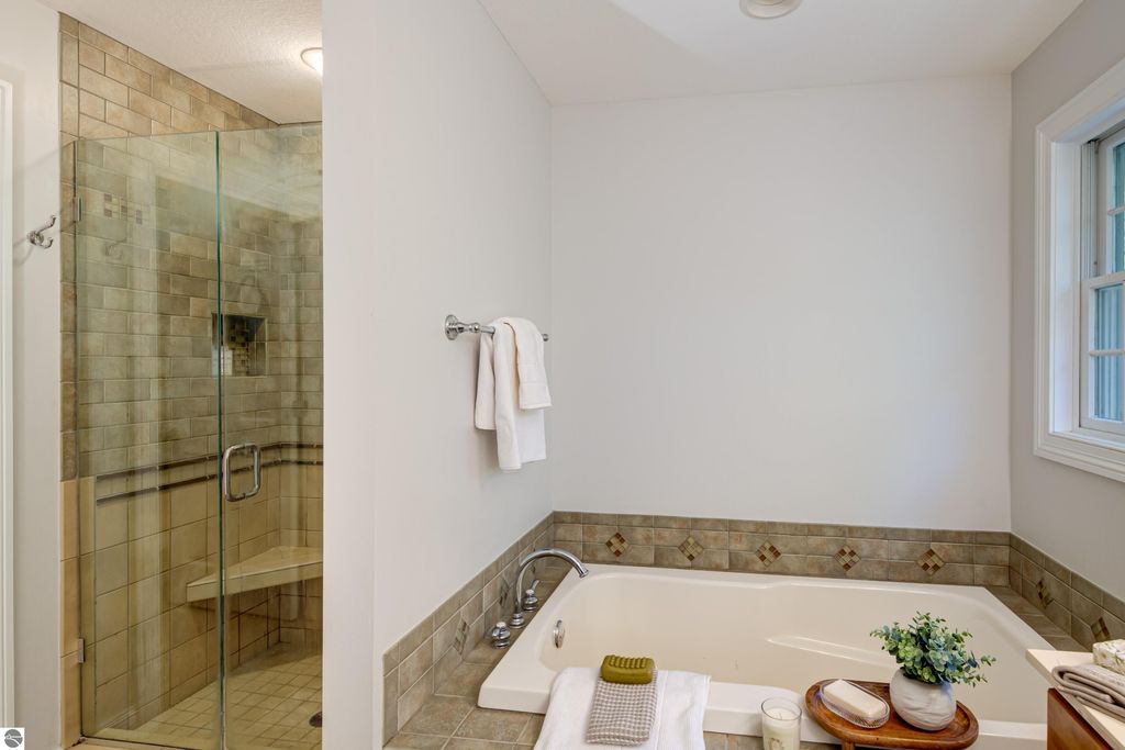 Luxurious bathroom featuring a walk-in glass shower, a spacious soaking tub, elegant tile work, and decorative accents, showcasing modern comfort and design at 6436 Peregrin Court, Traverse City, MI.