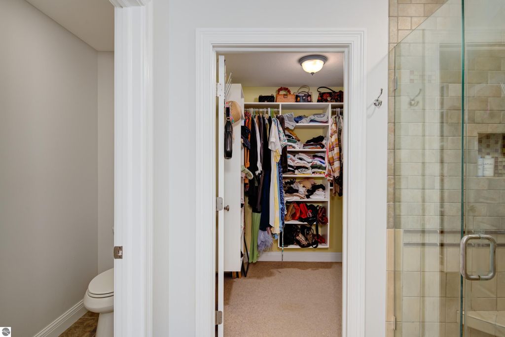 Walk-in closet with organized clothing racks, shelves filled with shoes and accessories, and a view of a glass shower, showcasing modern interior design elements in a Traverse City home for sale.