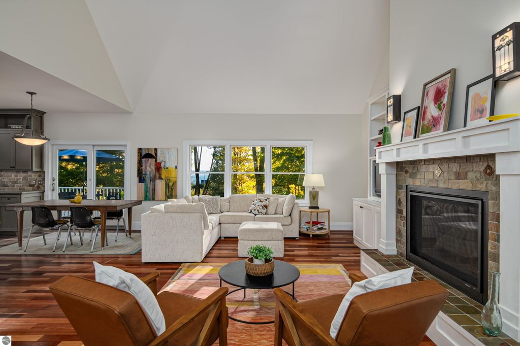 Modern living room with cozy seating, hardwood floors, and large windows showcasing views of East Bay, featuring a gas fireplace and dining area.