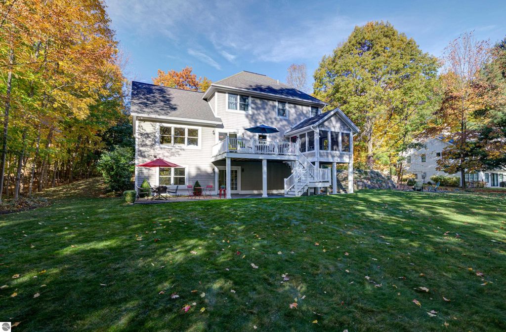 Custom-designed home at 6436 Peregrin Court, Traverse City, featuring a spacious backyard, deck with seating, and seasonal foliage, showcasing East Bay views and a park-like setting.