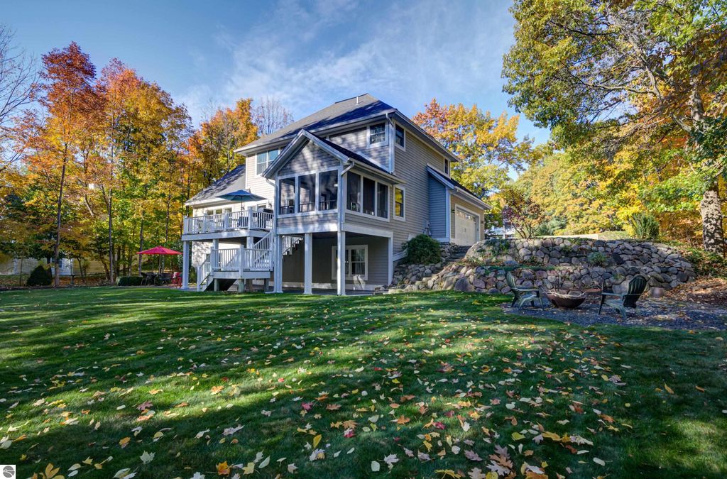 Custom-designed home at 6436 Peregrin Court, Traverse City, featuring a walkout lower level, three-season sunroom, and landscaped yard with fire pit, surrounded by vibrant autumn foliage.