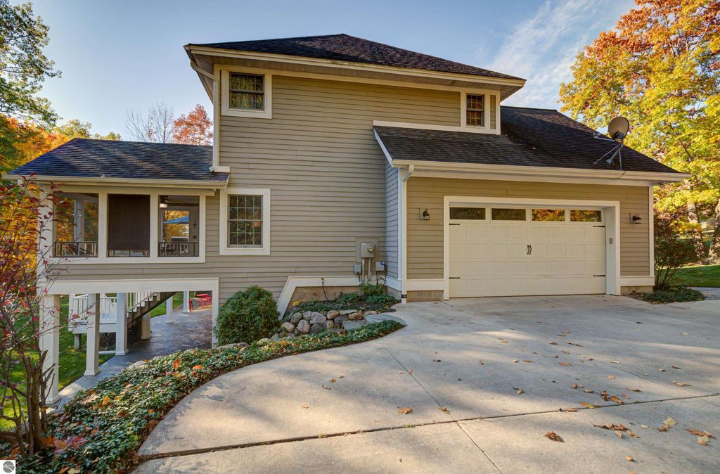 Custom-designed home exterior at 6436 Peregrin Court, Traverse City, showcasing a welcoming front porch, three-season sunroom, and landscaped yard with autumn foliage.