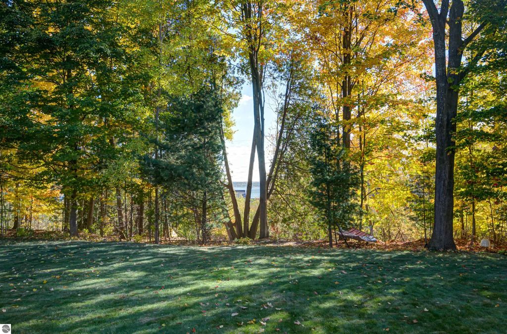 Scenic view of lush trees and vibrant fall foliage in the yard of 6436 Peregrin Court, showcasing a glimpse of East Grand Traverse Bay beyond.