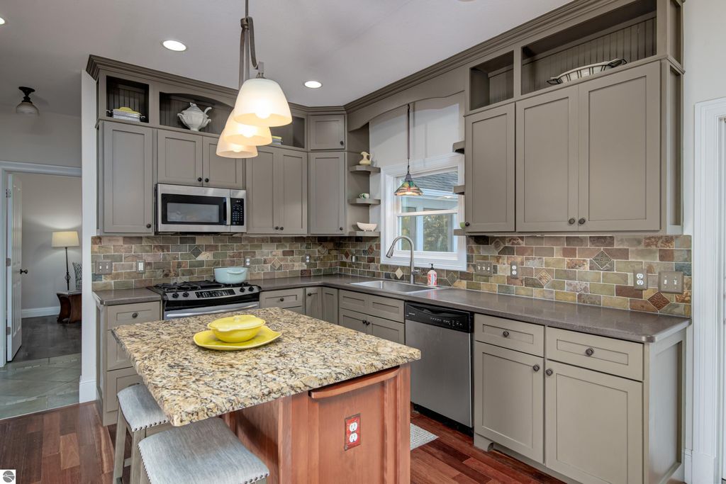 Modern kitchen featuring granite countertops, stainless steel appliances, and custom cabinetry, with a view of the adjoining living space, ideal for entertaining in the Traverse City home at 6436 Peregrin Court.