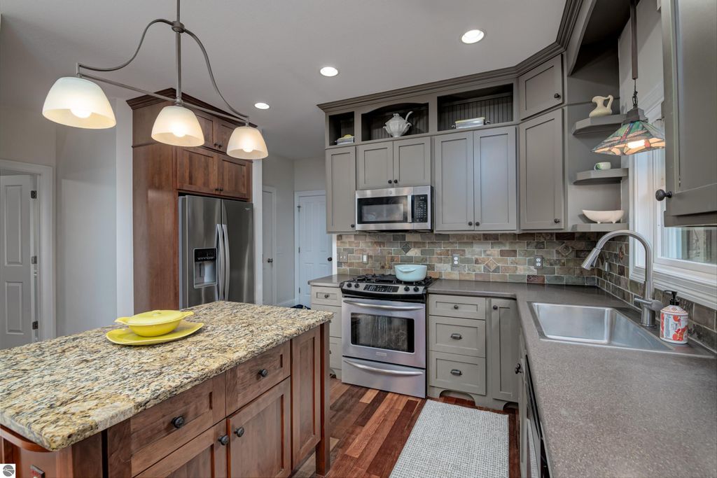 Modern kitchen with granite island, stainless steel appliances, wooden cabinetry, and decorative tile backsplash, showcasing a cozy and inviting atmosphere in the Traverse City home for sale.