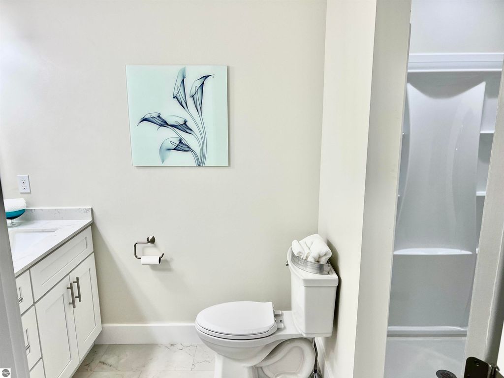 Modern bathroom featuring a white toilet, stylish vanity with marble countertop, and decorative wall art of floral design, showcasing a clean and inviting space in the home at 2757 Fashion Avenue, Interlochen, MI.