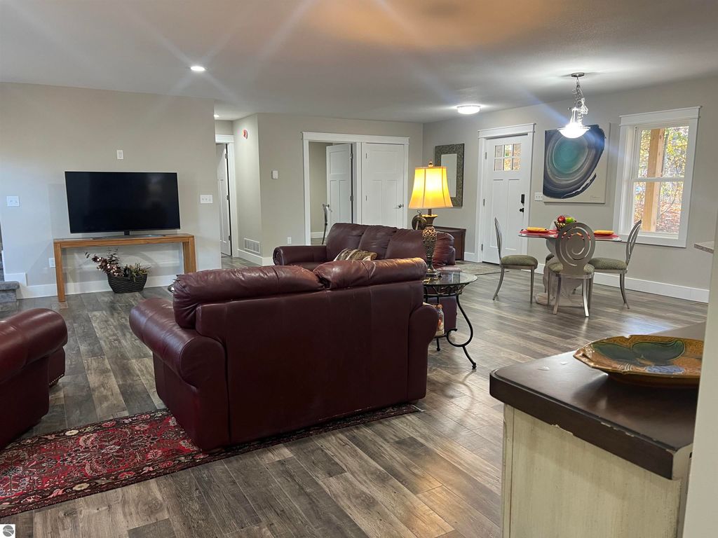 Cozy living room featuring burgundy leather sofas, a modern TV stand, and a dining area with a round table, highlighting a welcoming layout in the home at 2757 Fashion Avenue, Interlochen, MI.