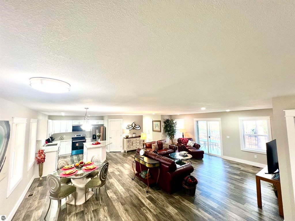 Spacious living area of a home in Interlochen, MI, featuring a modern kitchen with white cabinetry, dining table set for four, and a cozy lounge area with leather sofas, perfect for family gatherings and relaxation.