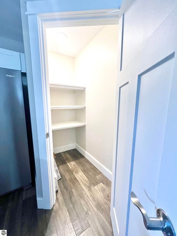 Interior view of a spacious pantry with white shelving, hardwood flooring, and a door partially open, showcasing organizational potential in the kitchen area of the home at 2757 Fashion Avenue, Interlochen, MI.